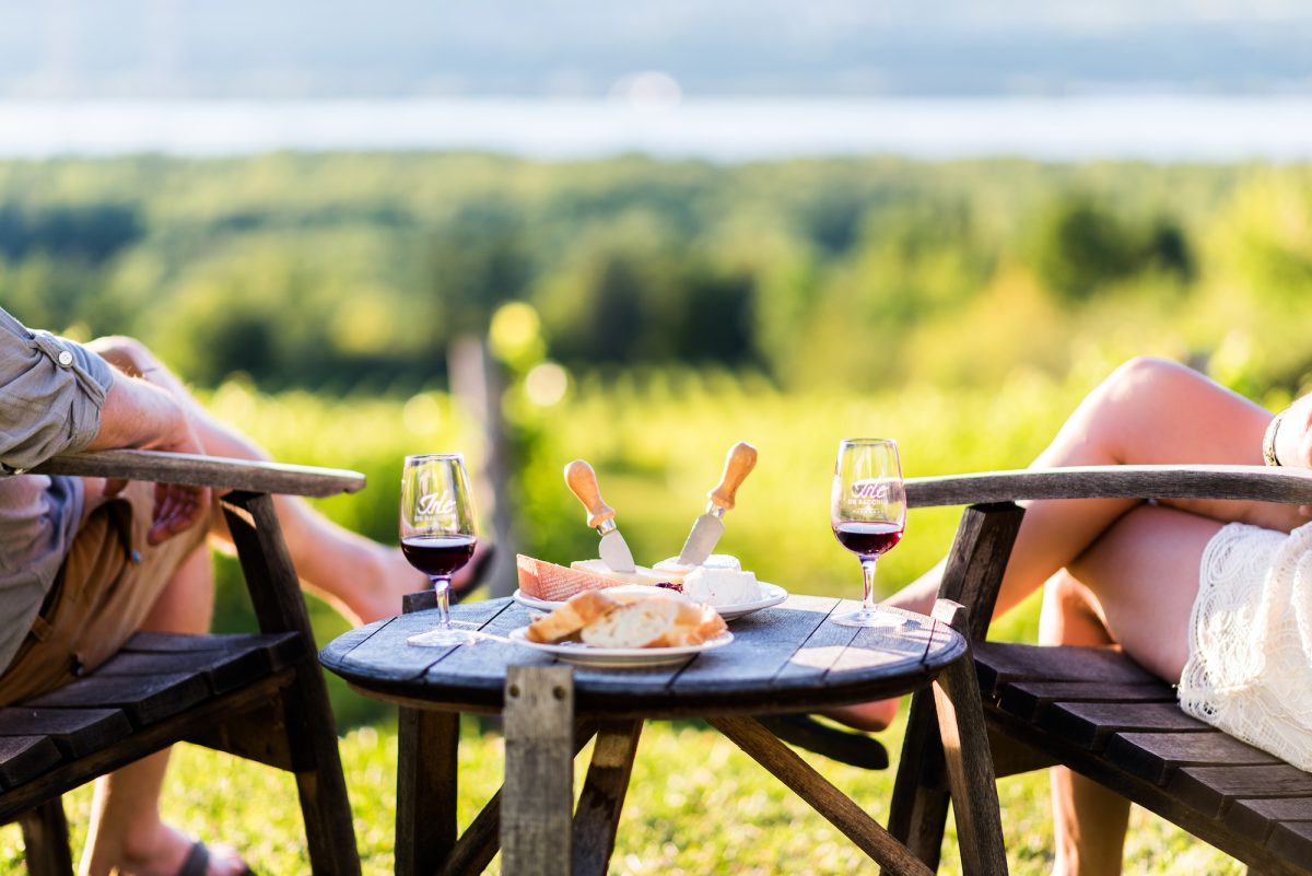 Pareja admirando la vista del St. Lawrence tomando vino y queso frente al viñedo de la Isla de Bacchus | Foto: Cortesía, rutas gastronómicas en Québec